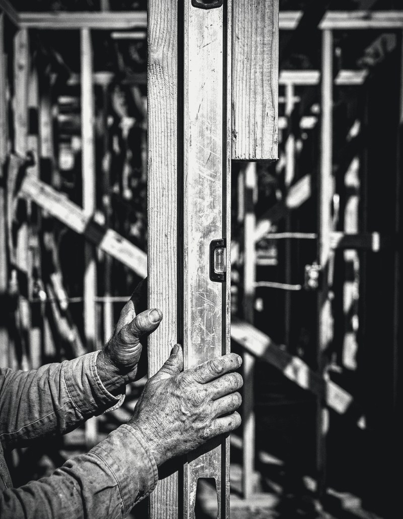 Hands holding a long level against a wall stud on a framed house