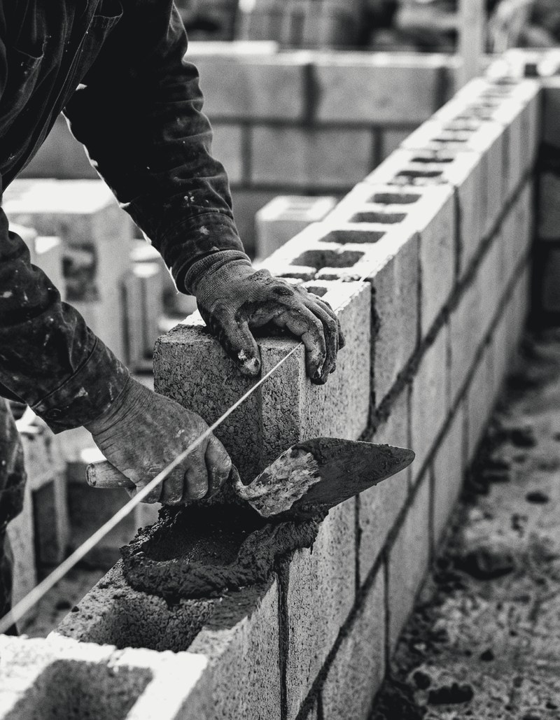 Mason setting a concrete block on a mortar bed to a string line