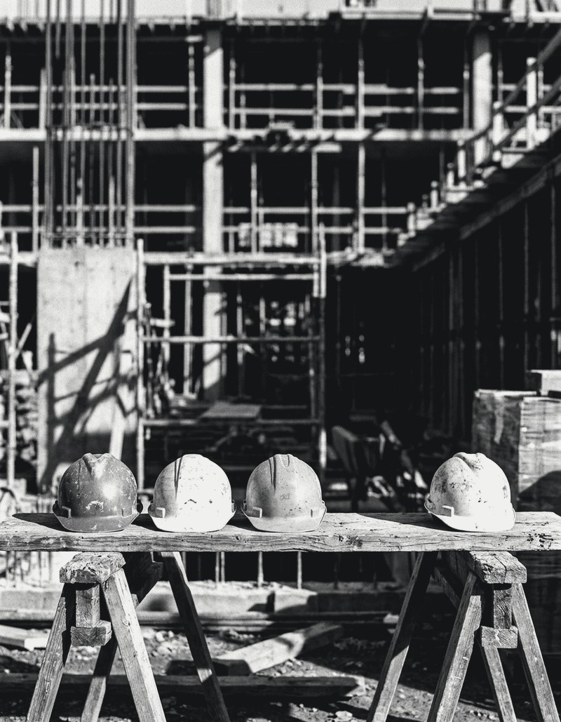 Four hard hats on a plank across sawhorses with a gap in the row, building under construction behind