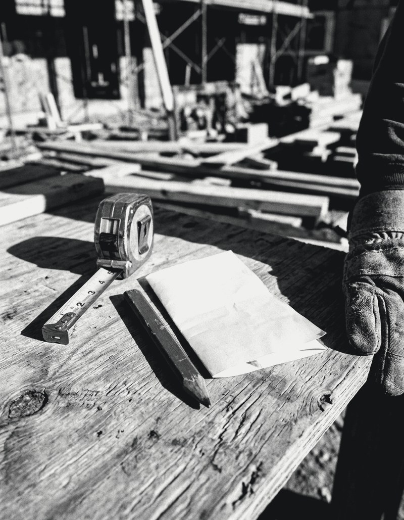 Carpenter pencil, folded estimate and tape measure on plywood, gloved hand at the edge